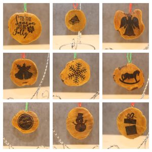 nine wood cookie ornament examples featuring different designs. From left to right, top to bottom; the words "Tis the season to be jolly" in script with a snowflake, two bells with the words "merry christmas", an angel silhouette, a silhouette of 2 bells with 3 holly leaves, a snowflake, a rocking horse silhouette, a framed circle with the words "merry christmas to you!", a snowman, and an open gift box silhouette