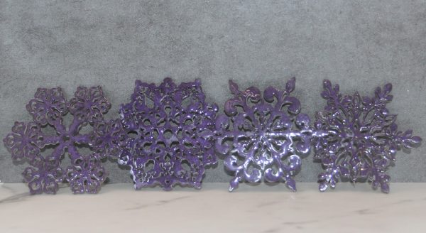4 sparkly purple snowflake shaped coasters, each a different shape, lined up next to each other, leaning on a gray background