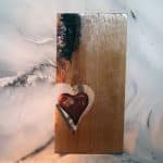 Handcrafted wood heart art — live edge oak slab with natural dark edge and suspended padauk heart held together with copper plate, copper wire stitching, and screws, inspired by the Perfect Heart parable