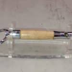 Handturned wooden whistle keychain with reclaimed hardwood body and polished stainless steel fittings, displayed on clear acrylic stand, approximately 3 inches long, made by veteran artisan Sar Cowan at Sarkanys Rising in Tucson Arizona