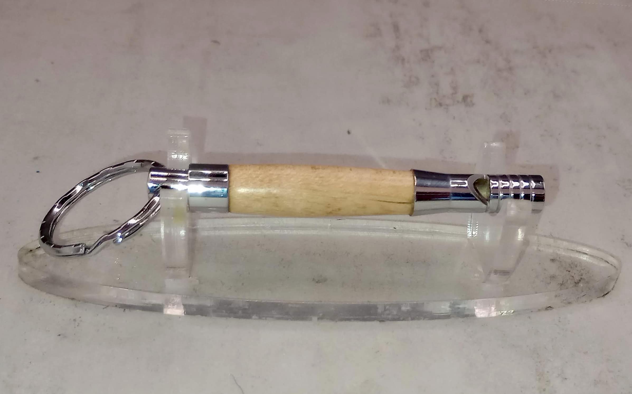 Handturned wooden whistle keychain with reclaimed hardwood body and polished stainless steel fittings, displayed on clear acrylic stand, approximately 3 inches long, made by veteran artisan Sar Cowan at Sarkanys Rising in Tucson Arizona