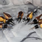Eight hand-turned dark and light bottle stoppers fanned out on marble background showing full contrast wood collection of artisan bar gifts by Sarkanys Rising Tucson