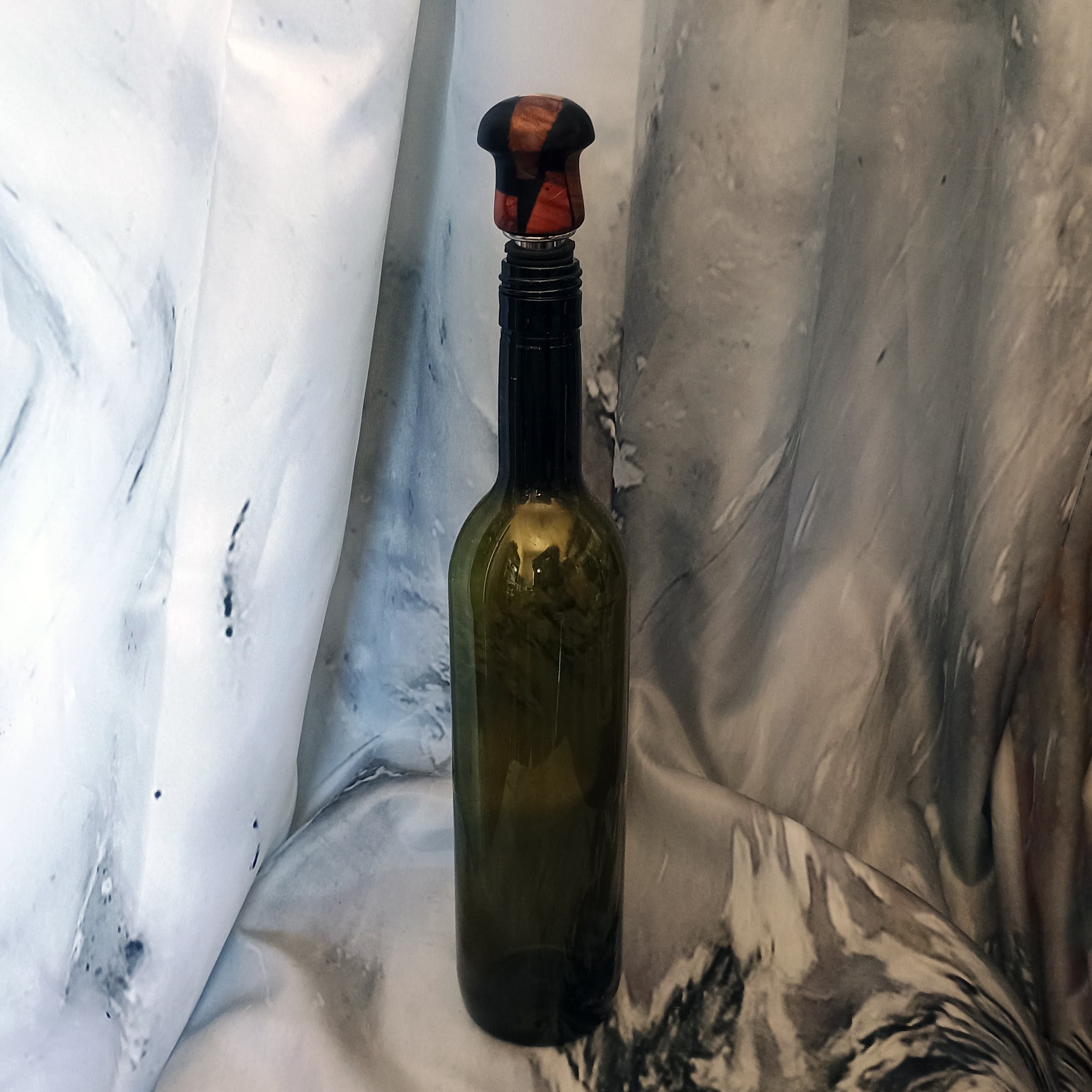 Hand-turned droplet bottle stopper with scrap wood and black resin cap seated in a dark green wine bottle, artisan bar gift by Sarkanys Rising