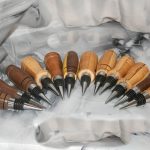 Thirteen hand-turned scrap wood bottle stoppers fanned out on marble background showing full collection of artisan hardwood bar gifts by Sarkanys Rising Tucson