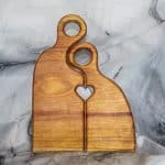 Front view of a canary wood Romeo and Juliet cutting board set with carved heart cutout and S-curve interlocking handles, canary wood Romeo Juliet cutting board by Sarkanys Rising